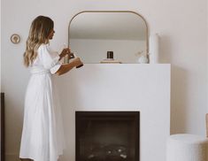 a woman standing in front of a fire place with a mirror on the wall above it