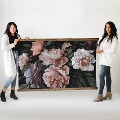 two women holding up a large floral print on a white background with one woman standing next to the frame