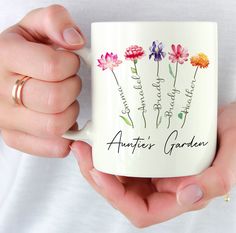 a woman is holding a coffee mug with flowers on it and the words, another garden written in cursive writing