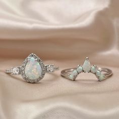 two opal and diamond rings sitting on top of a white satin surface, with one ring in the shape of an arrow