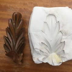 two pieces of white clay sitting on top of a wooden table next to a leaf shaped object