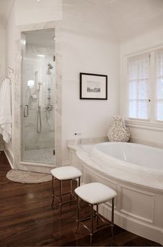 a large white bathroom with a walk in shower next to a bathtub and two stools