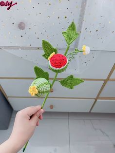 a hand holding a crocheted flower in front of a white ceiling with stars and confetti on it