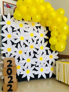 a room decorated with yellow balloons and white daisies on the wall, next to a sign that reads 2012