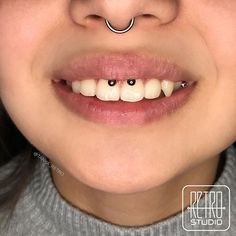 a woman with black nose piercings and white teeth