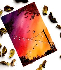 a card with string lights and leaves on the ground next to it is an image of birds flying in the sky