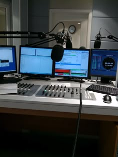 three computer monitors sitting on top of a desk next to headphones and microphones