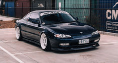 a black sports car parked in a parking lot next to a fence and some buildings