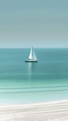 a sailboat is out on the open water near an empty beach with white sand