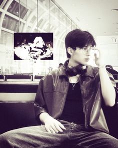 a young man sitting on top of a chair talking on a cell phone while wearing glasses