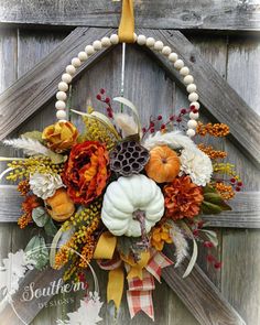 a wreath with pumpkins, flowers and feathers hanging on a wooden door frame in front of a barn