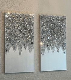 two silver and white paintings on a wall next to each other with lights in them