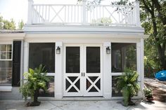 a white house with black shutters and two large plants on the front porch area