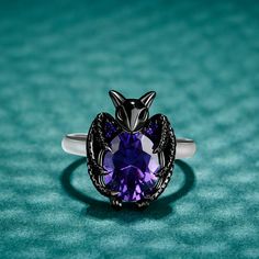 Give wings to your night, make your style with this bat ring that is both fashionable and cool. Crafted in sterling silver, this ring shows a little black bat hugging an oval-cut purple stone with its wings. The bat flying in the dark symbolizes wisdom and courage. This black bat ring is like an elf on your finger, full of mystery. It's a special gift to her as halloween jewelry or vampire bat jewelry worn on halloween or any party.Carat Weight: 3 ctStone Size: 8*10 mmStone Type: Jeulia® StoneNu Bat Ring Jewelry, Vampiric Jewelry, Purple Rings Engagement, Vampire Rings, Bat Ring, Bat Jewelry, Skull Engagement Ring, Bat Flying, Purple Rings