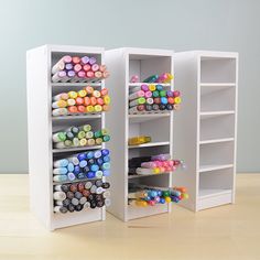 two white shelves with different colored crayons in them on top of a wooden table