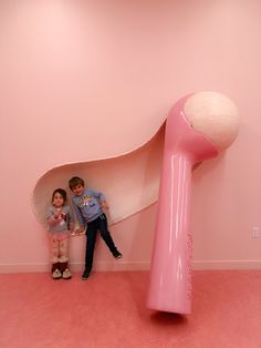 two children are sitting next to a giant pink object in the shape of a hairdryer