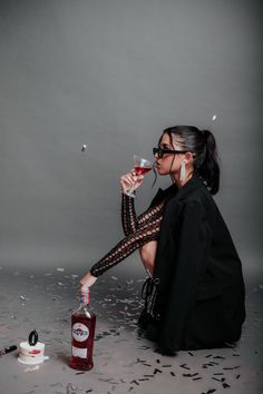 a woman sitting on the ground with a bottle of alcohol in her hand and confetti falling around her