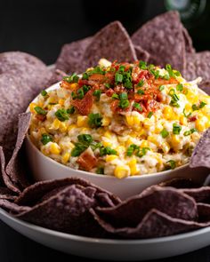 a white bowl filled with corn, bacon and green onions surrounded by tortilla chips