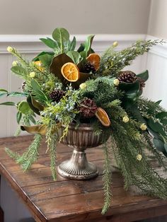 a vase filled with greenery and oranges on top of a wooden table