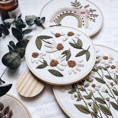 three embroidery hoops with flowers and leaves on them next to a bottle of alcohol