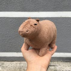 a hand holding a small stuffed animal in front of a gray wall with white stripes