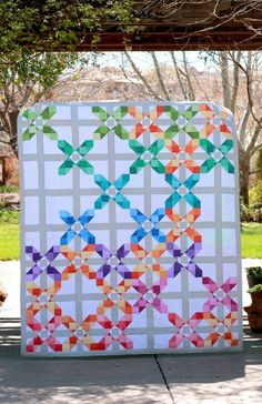 a colorful quilt is hanging on the side of a building with trees in the background