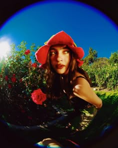 a woman wearing a red hat and holding a rose in front of her face while looking at the camera