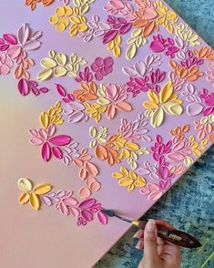 someone is cutting out paper flowers on a piece of pink and yellow art with scissors