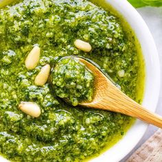 a white bowl filled with pesto sauce and a wooden spoon on top of it