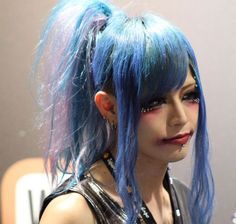 a woman with blue hair and makeup looks at her cell phone