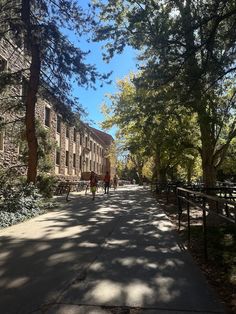 two people are walking down the sidewalk in front of some buildings and trees on a sunny day