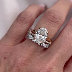 a woman's hand with two engagement rings on top of her ring and the middle one has an oval shaped diamond