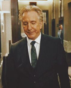 a man in a suit and tie walking down a hall way with his eyes closed