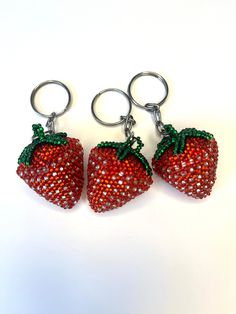 three strawberry keychains are shown on a white surface