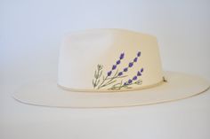 a white hat with purple flowers on the brim and side, against a white background