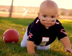 a baby is wearing a football jersey and sitting in the grass next to two balls