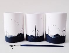 three coffee cups with windmills painted on them next to a brush and ink pen