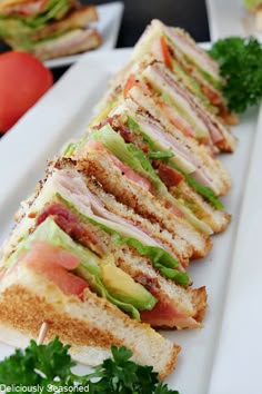 a sandwich cut in half sitting on top of a white plate next to tomatoes and lettuce