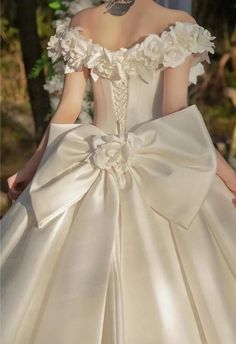 a woman in a white wedding dress with flowers on the shoulder and large bow at the waist