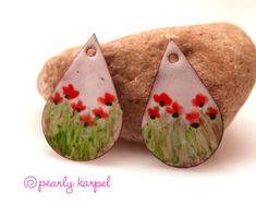 the earrings are decorated with red flowers and green grass, on top of a rock