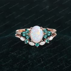 an opal and diamond ring on a black surface with green stones in the middle