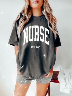 "FREE SHIPPING IN THE US! No order minimum!  Comfort Colors Nurse Shirt, Nurse Shirtk, Nurse Est 2024, Graduation Gift for Nurse, Nurse Shirt Gift, Nurse Tshirt, Gift for New Nurse ♥ The SHIRT This is a Comfort Colors 1717 shirt.  * This unisex t-shirt is intended to be loose/oversized for women to give a chic and laid back vibe. If you are looking for an oversized \"T-shirt Dress\" look, we recommend sizing up 2-3 sizes.  * Detailed sizing information can be found in the size chart in the photos.  * Printed in the USA. ♥ CARE  ＊Machine wash cold, inside-out, gentle cycle ＊Wash with mild detergent and similar colors ＊Tumble dry low or hang-dry ＊Do not bleach or fabric softeners ＊Do not iron directly onto the design ＊Do not dry clean ♥ PRODUCTION & SHIPPING ＊Each shirt is made to order. ＊Pr School Spirit Short Sleeve T-shirt With Letter Print, Oversized School Spirit T-shirt With Letter Print, Black Tops With Team Name Relaxed Fit, Short Sleeve Tops For School Spirit Streetwear, Black Relaxed Fit Top With Team Name, Black Short Sleeve School Spirit Top, College Tops With Graphic Print And Relaxed Fit, Relaxed Fit Graphic Print Top For College, College Graphic Print Top With Relaxed Fit