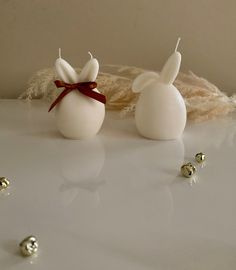 two white candles with red bows on them sitting next to some balls and feathers in the background