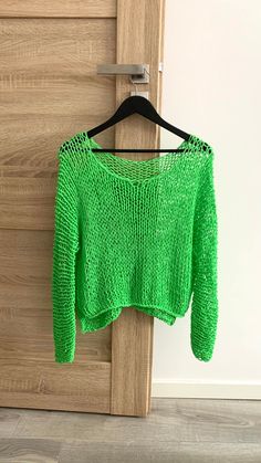 a green sweater hanging on a wooden door with a hanger in front of it