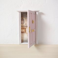 an open pink door on top of a wooden table next to a white wall and floor