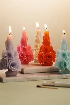 five candles with different colored flowers on them next to a notebook and pencils in the background