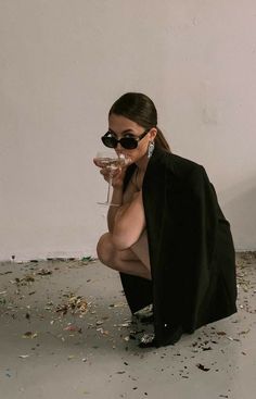 a woman kneeling on the ground drinking from a wine glass with confetti all around her