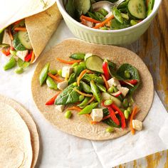 two tortillas filled with veggies on top of a wooden table next to a bowl of salad