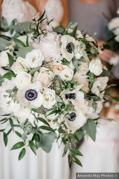 a bridal bouquet with white flowers and greenery is held by two bridesmaids