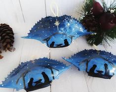 three blue glass dishes with silhouettes on them and pine cones in the foreground